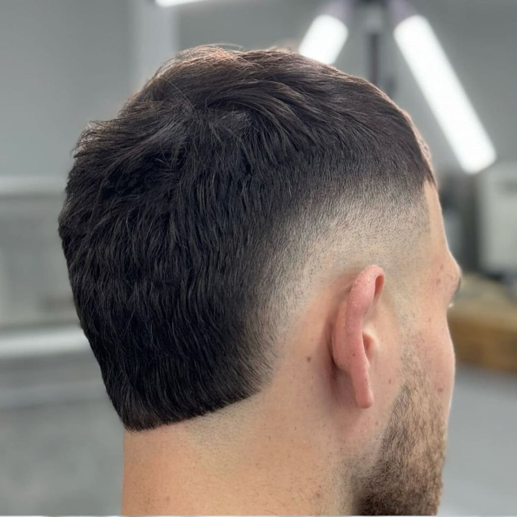 Back view of a Classic Short Hair Burst Fade showcasing a clean, seamless transition from a sharp skin fade to a fuller textured top. The fade curves smoothly around the ears, creating a rounded and polished look. Ideal for men seeking a timeless and low-maintenance style that emphasizes clean lines and modern grooming. This haircut highlights precision and versatility, making it perfect for various occasions.