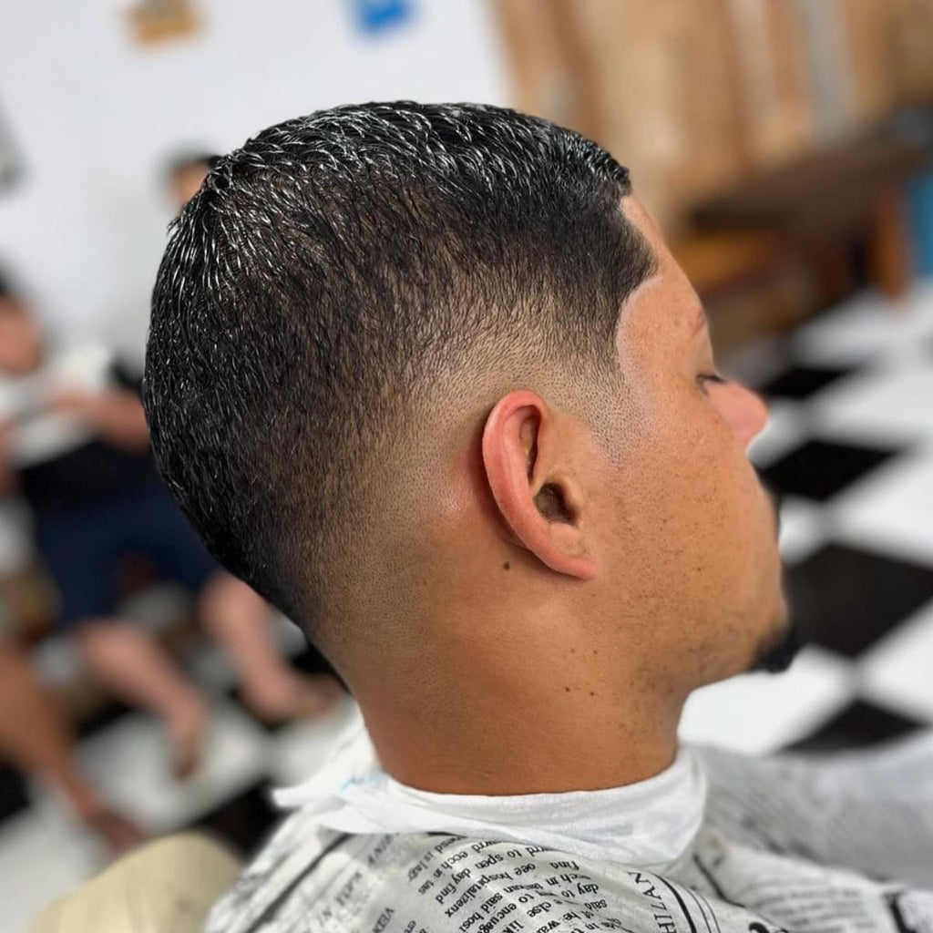 Side view of a man with a clean mid fade buzz cut, showcasing a smooth, gradual fade that blends seamlessly from the short sides to the slightly longer top. The haircut has a precise, tapered finish that emphasizes the neatness and structure of the mid fade. Ideal for a low-maintenance, stylish look, this cut enhances the natural hair texture while keeping a polished appearance.