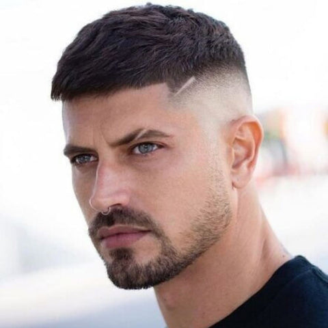 Man with a modern Crew Cut, featuring a short, textured top and a sharp skin fade on the sides. The hairstyle is accentuated with a subtle hairline design, adding a contemporary twist to this classic short hairstyle for men. The look is completed with a neatly groomed beard, creating a stylish and confident appearance.