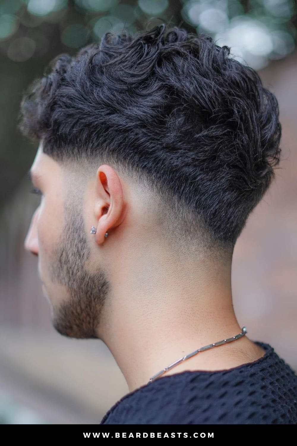 This image features a stylish curly low fade haircut, where the hair transitions smoothly from fuller curls on top to a closely cropped, tapered fade at the sides and back. The fade starts just above the ears, blending seamlessly into the natural curls, creating a clean and modern look. This haircut is perfect for highlighting the texture of curly hair while maintaining a sleek, low-maintenance style. Ideal for those seeking a balance between a sharp fade and defined curls.