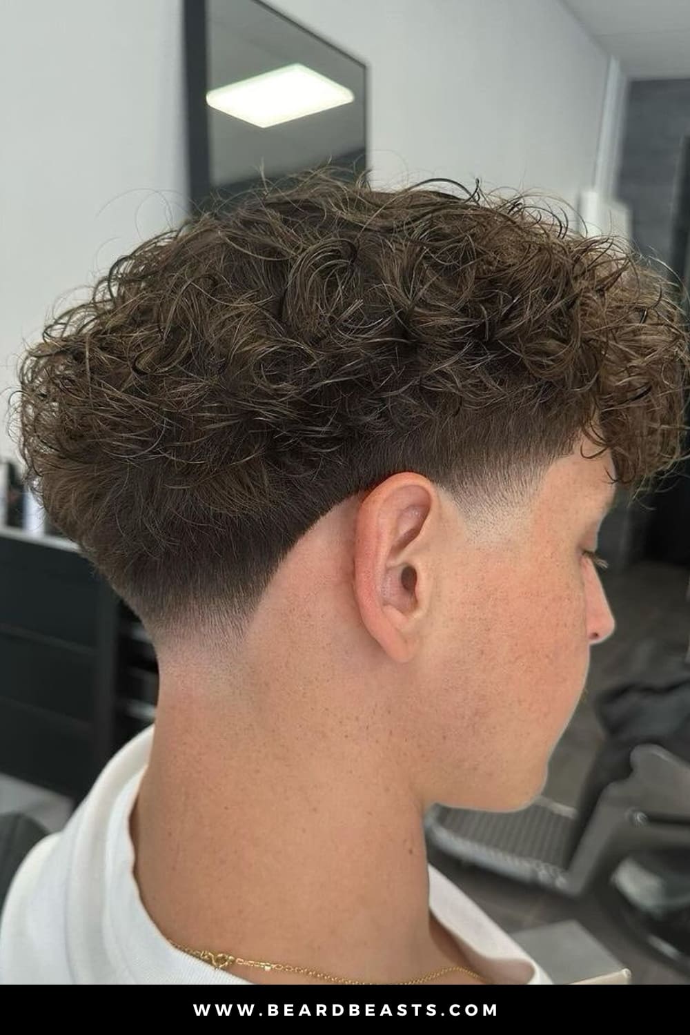 A close-up image of a stylish curly taper fade haircut. The hair on top features soft, voluminous curls, gradually tapering down to a clean fade at the sides and back of the head. This curly taper fade offers a sharp contrast between the thick curly texture and the neatly faded sides, making it a popular and modern choice for those with curly hair looking for a fresh, low-maintenance style. Ideal for enhancing natural curls while keeping the sides sleek and neat.