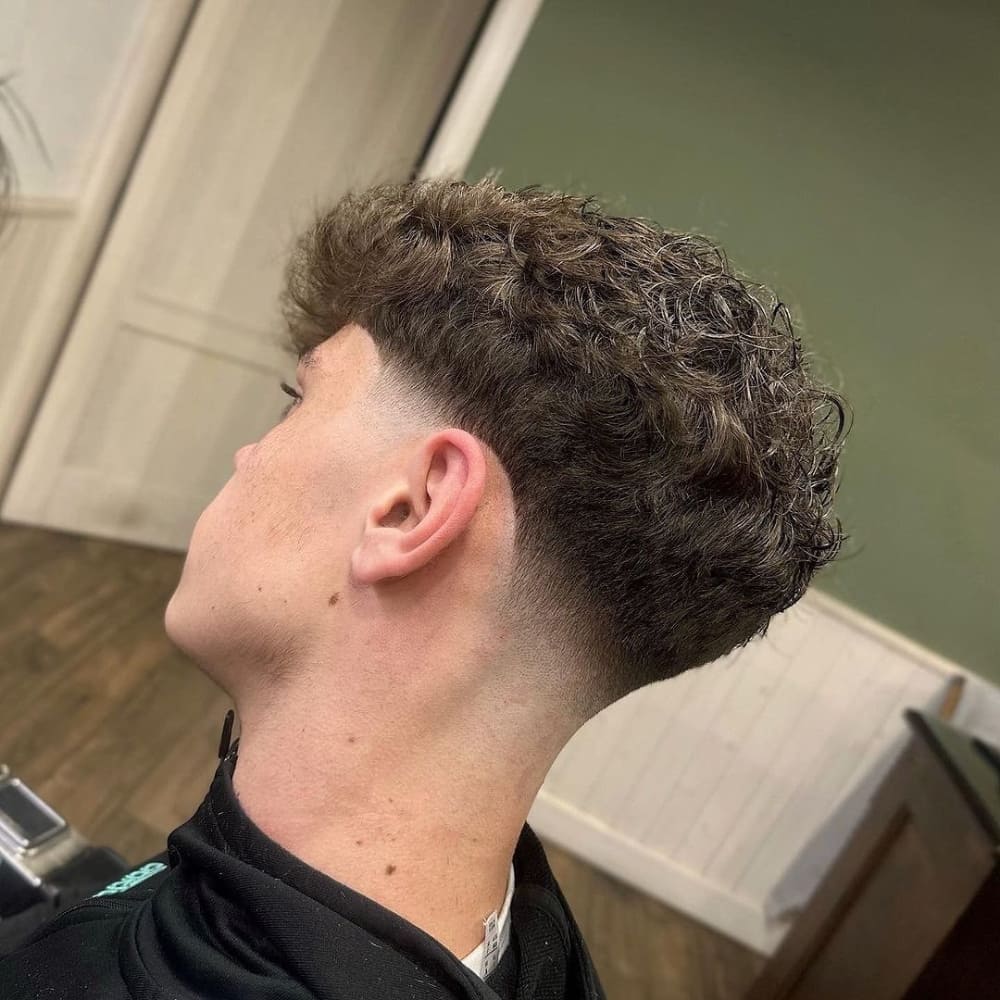 Man with a curly top low fade haircut, featuring naturally curly hair on top and a clean fade on the sides and back, showcasing a stylish and modern look for 2024.