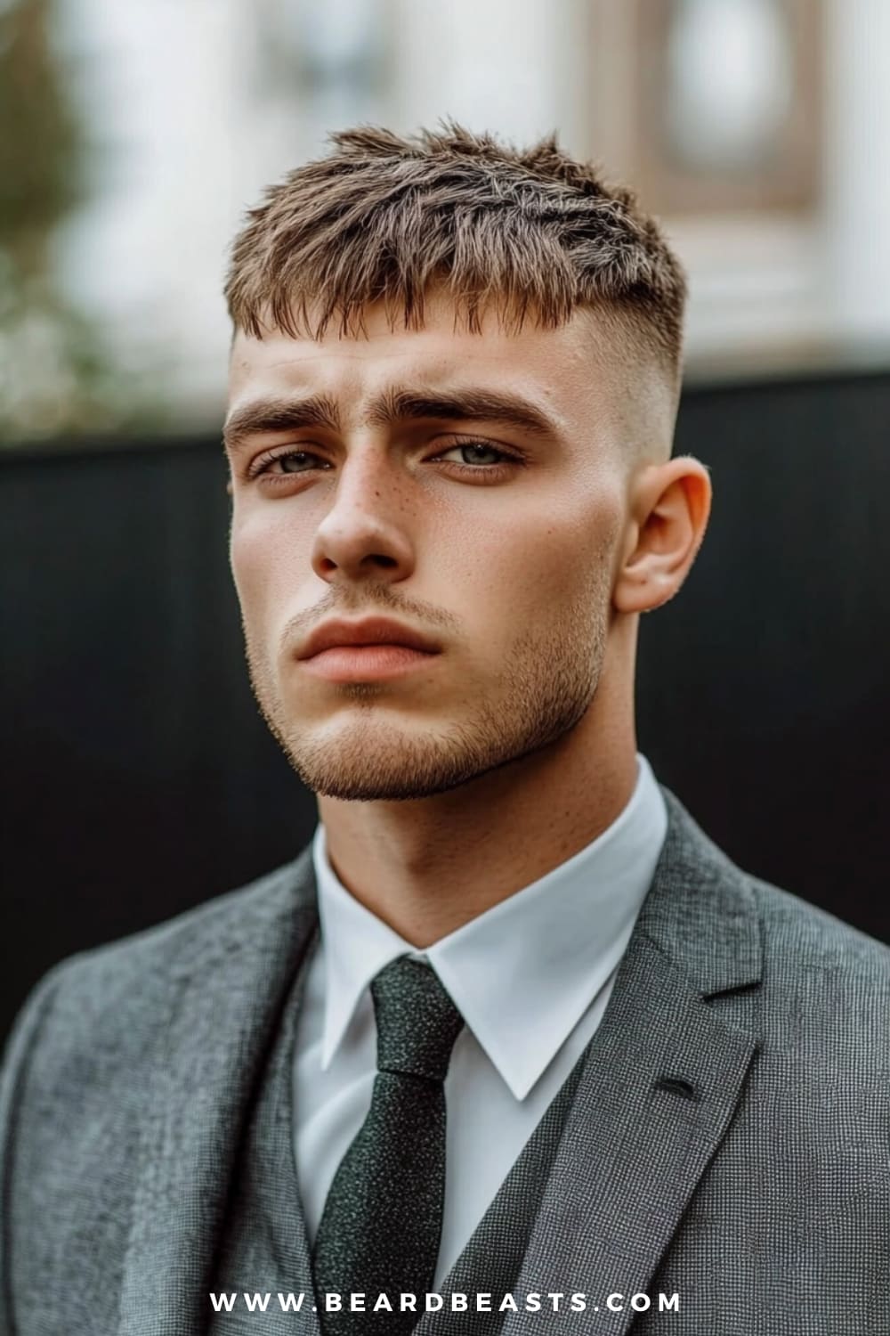 A young man confidently showcases a stylish French crop, one of the go-to short hairstyles for men with thick hair. His thick hair is textured and cropped short on top, with a blunt fringe that adds a modern edge to the look. The sides are neatly faded, creating a clean and sharp contrast that highlights his facial features.