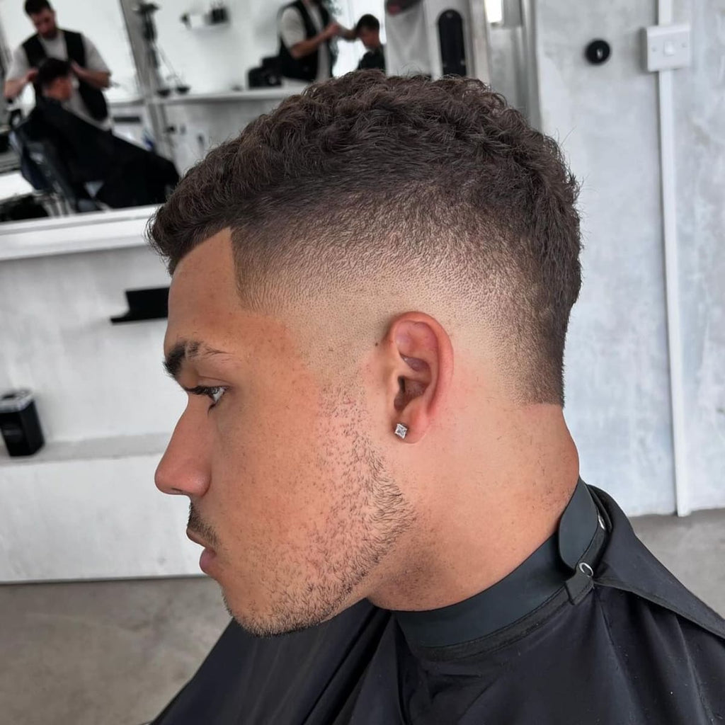 Side profile of a man with a fresh, curly haircut featuring a smooth fade and clean, tapered edges. The short, defined curls on top complement the sharp, faded sides, giving a polished and stylish look.