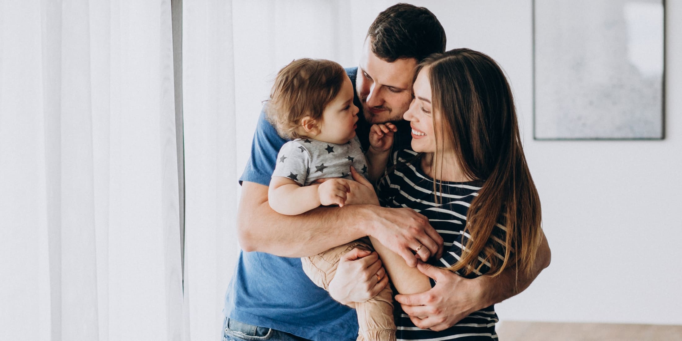 Happy family scene featuring a father, mother, and young child sharing a warm embrace in a bright, airy room. This image reflects the importance of a balanced life, highlighting the value of family time, work-life balance, and nurturing close relationships. The natural lighting and simple background emphasize the joy and connection within the family unit.