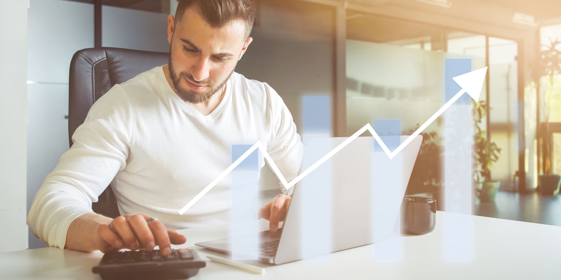 Man sitting at a desk, focused on financial work with a calculator and laptop, while a graphical representation of rising bar charts and an upward arrow overlays the image. This image embodies habits for financial success, emphasizing the importance of budgeting, smart spending, and investing. The upward trend in the graph symbolizes growth, progress, and the effective management of finances.