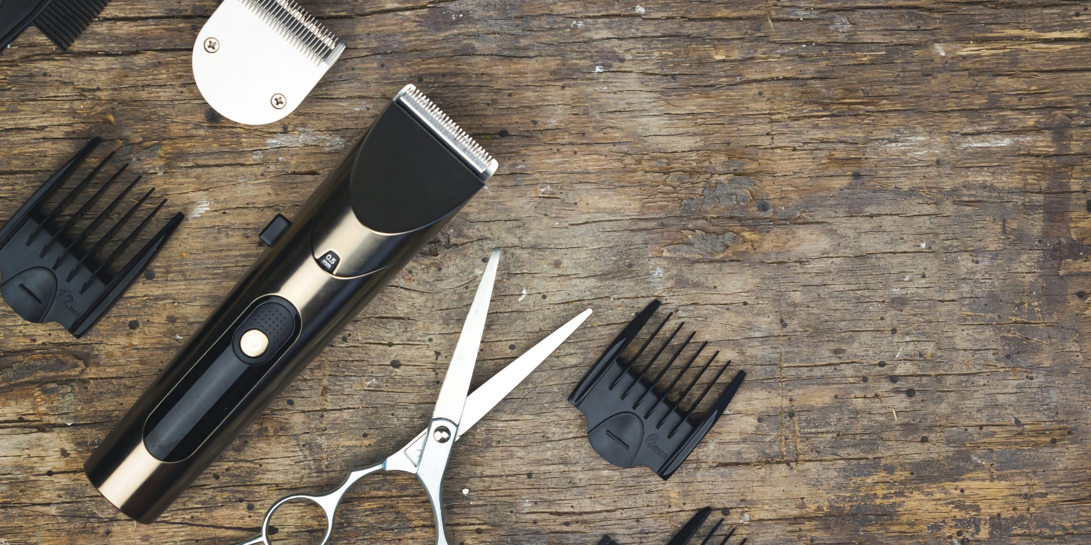 Hair clipper set including clippers, guards, and scissors on a wooden background, illustrating how to clean hair clippers for optimal performance and hygiene.