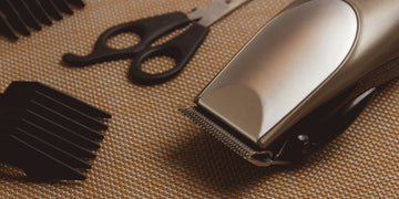 Hair clipper set with scissors and attachment guards on a textured surface, demonstrating the steps on how to clean hair clippers for best performance and hygiene.