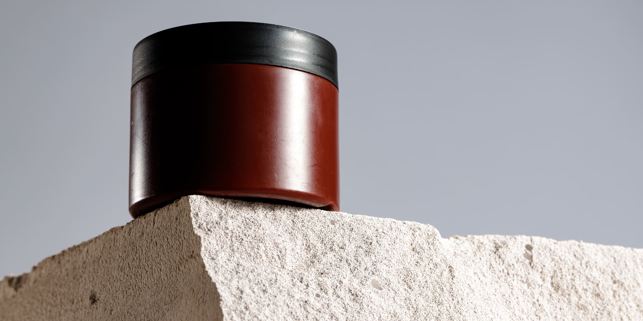 Modern jar of hair wax on a textured rock surface. The dark brown jar with a black lid is perfect for achieving a natural, textured look. Ideal for various hair types and lengths, highlighting the benefits of hair gel vs wax in hair styling products.