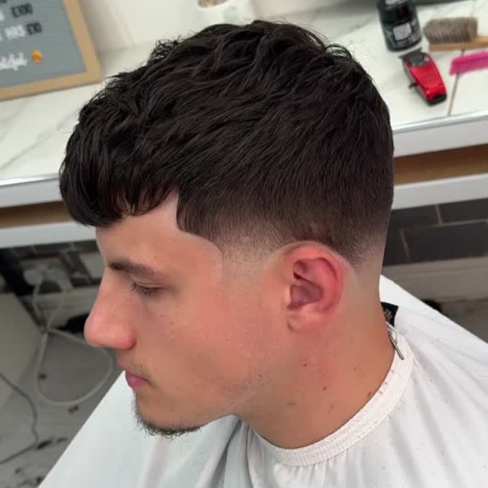 Man with a high taper crop haircut, featuring a short, blunt cut on top with neatly tapered sides. The style showcases a clean, defined hairline and a subtle goatee, creating a polished and modern look