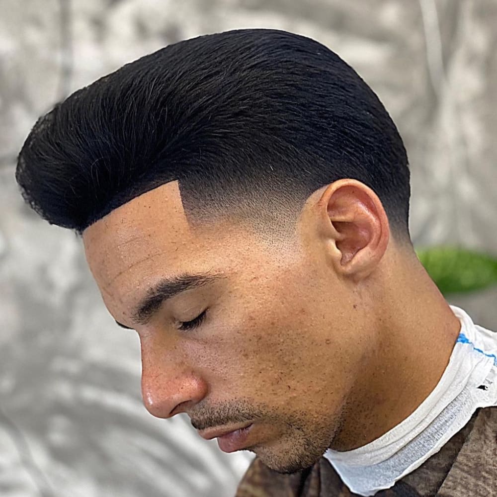 Man with a high taper pompadour haircut, featuring a voluminous top and neatly tapered sides. The haircut highlights a sharp, clean hairline and a smooth, polished finish.