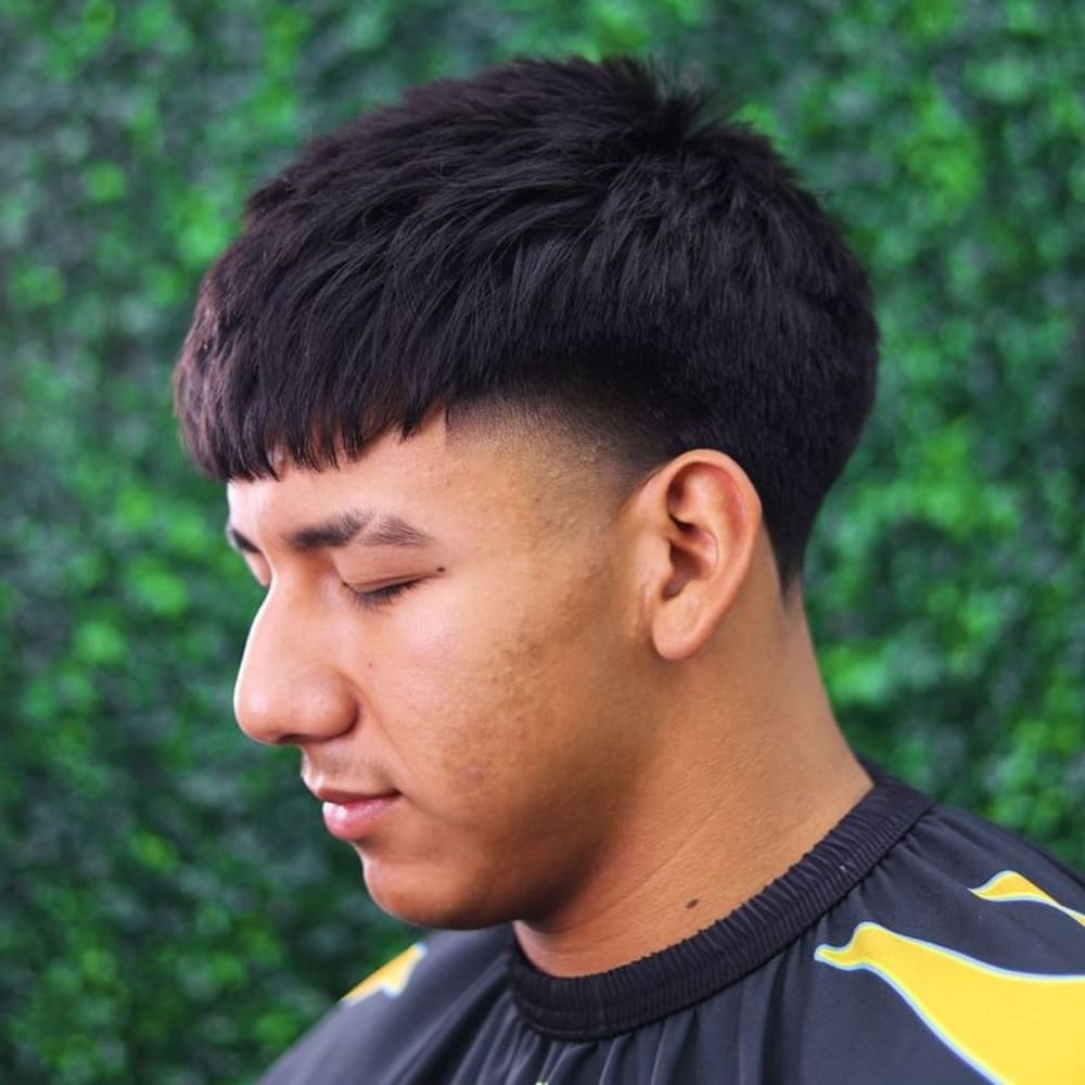 Man with a high taper haircut featuring a textured fringe. The style showcases a choppy, layered fringe that adds volume and movement, along with sharply tapered sides for a clean and modern look.