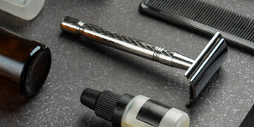 Close-up of a safety razor with cleaning tools, including a dropper bottle and comb, on a dark surface. Essential items for learning how to clean a safety razor effectively for a smooth and hygienic shave.