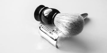 Close-up of a shaving brush with soft bristles and a classic safety razor on a white background, demonstrating essential grooming tools. Learn how to clean a shaving brush effectively for a hygienic and long-lasting shaving experience.