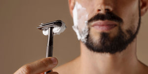  Man preparing to learn how to get a close shave with a safety razor, shaving cream on his face, focused on achieving a smooth shave. 