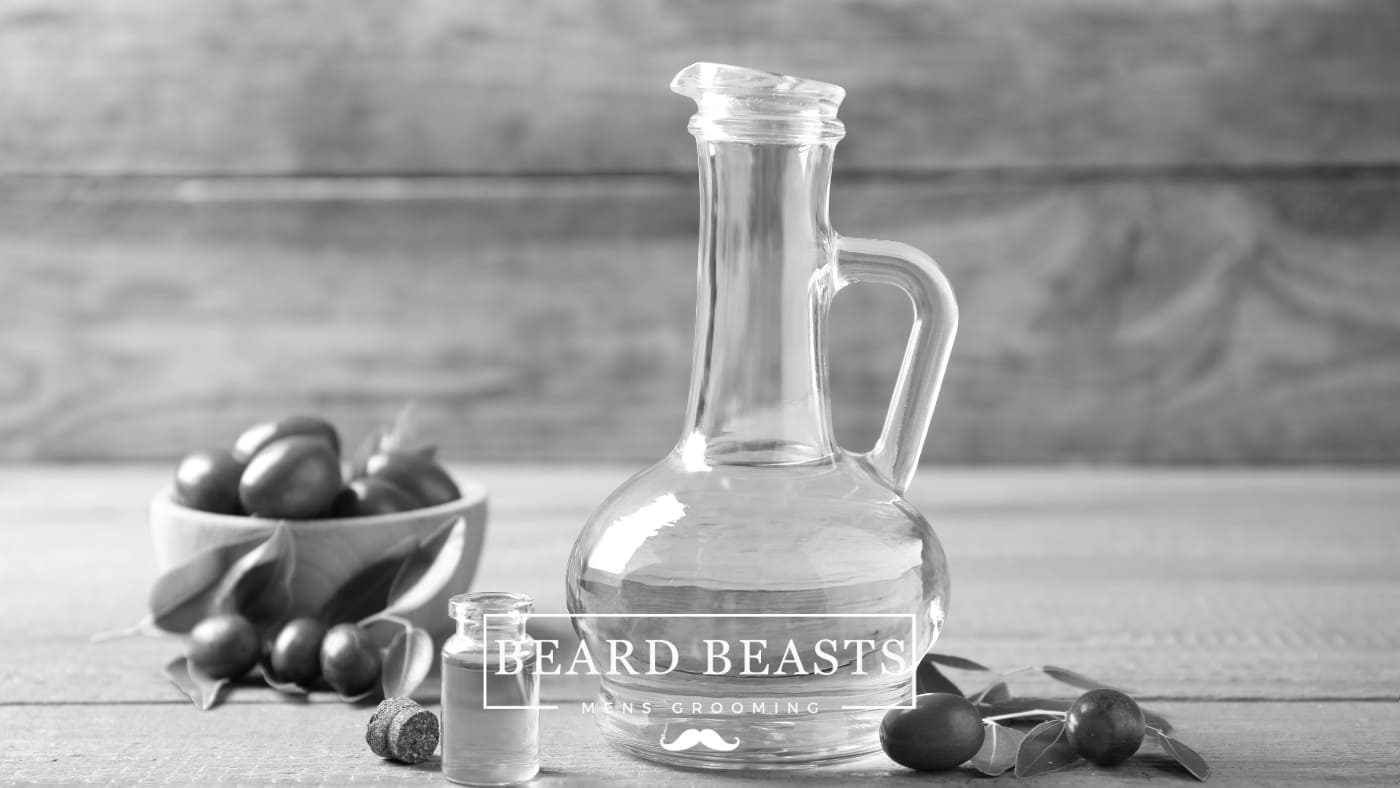 Bowl of fresh jojoba seeds and leaves with a glass jug and dropper bottle of jojoba oil for beard care