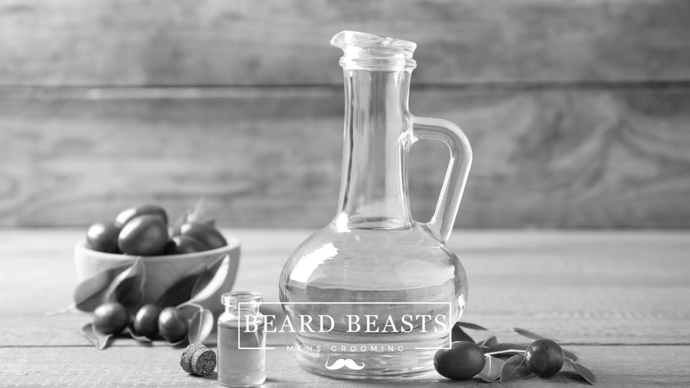 Bowl of fresh jojoba seeds and leaves with a glass jug and dropper bottle of jojoba oil for beard care