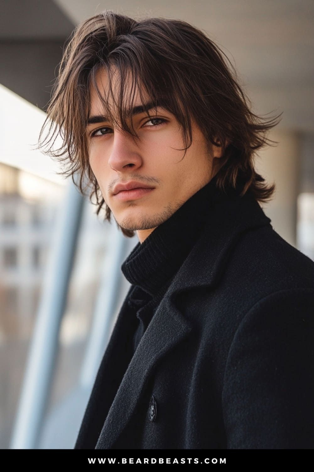 Man with long, textured hair and bangs, wearing a black coat, exuding a chic and modern look. The layered bangs and flowing locks create a stylish, sophisticated appearance, making it a prime example of men's hairstyles for long hair that balance texture and elegance.