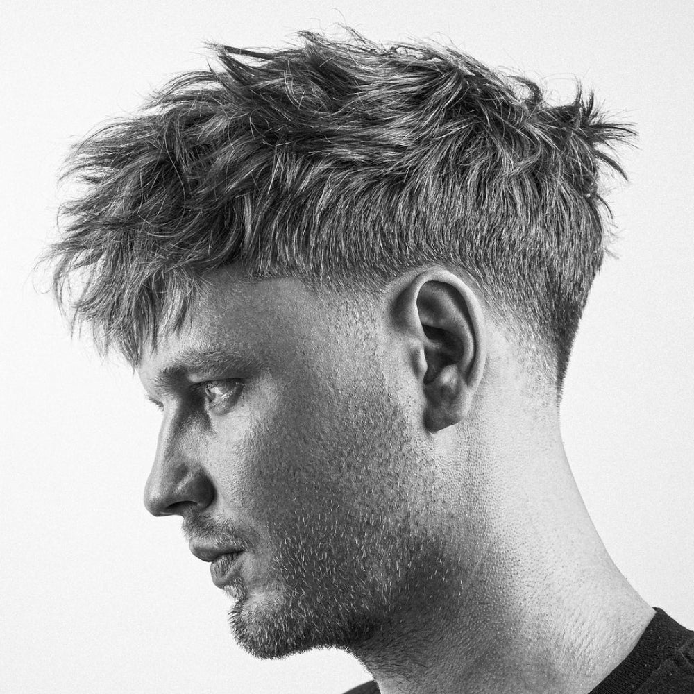 Man with a low fade messy top haircut, featuring textured, tousled hair on top and a clean fade on the sides and back, highlighting a modern, trendy look for 2024.