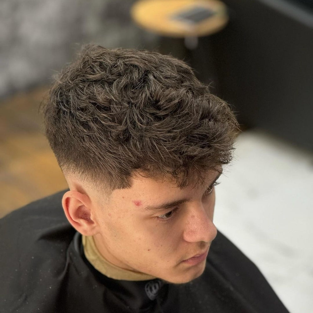 Man with a low fade haircut and textured top, featuring short, cleanly faded sides and back with a voluminous, textured hairstyle on top, showcasing a trendy and modern look for 2024.