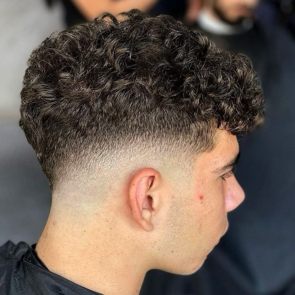 Young man with a low fade haircut featuring naturally curly hair, showcasing a clean and stylish look perfect for various hair types and face shapes.