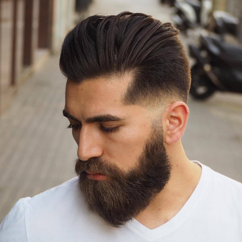 Man with a low fade haircut and full beard, featuring a sleek and voluminous top paired with a sharp fade and a thick, well-groomed beard, showcasing a stylish and masculine look for 2024.