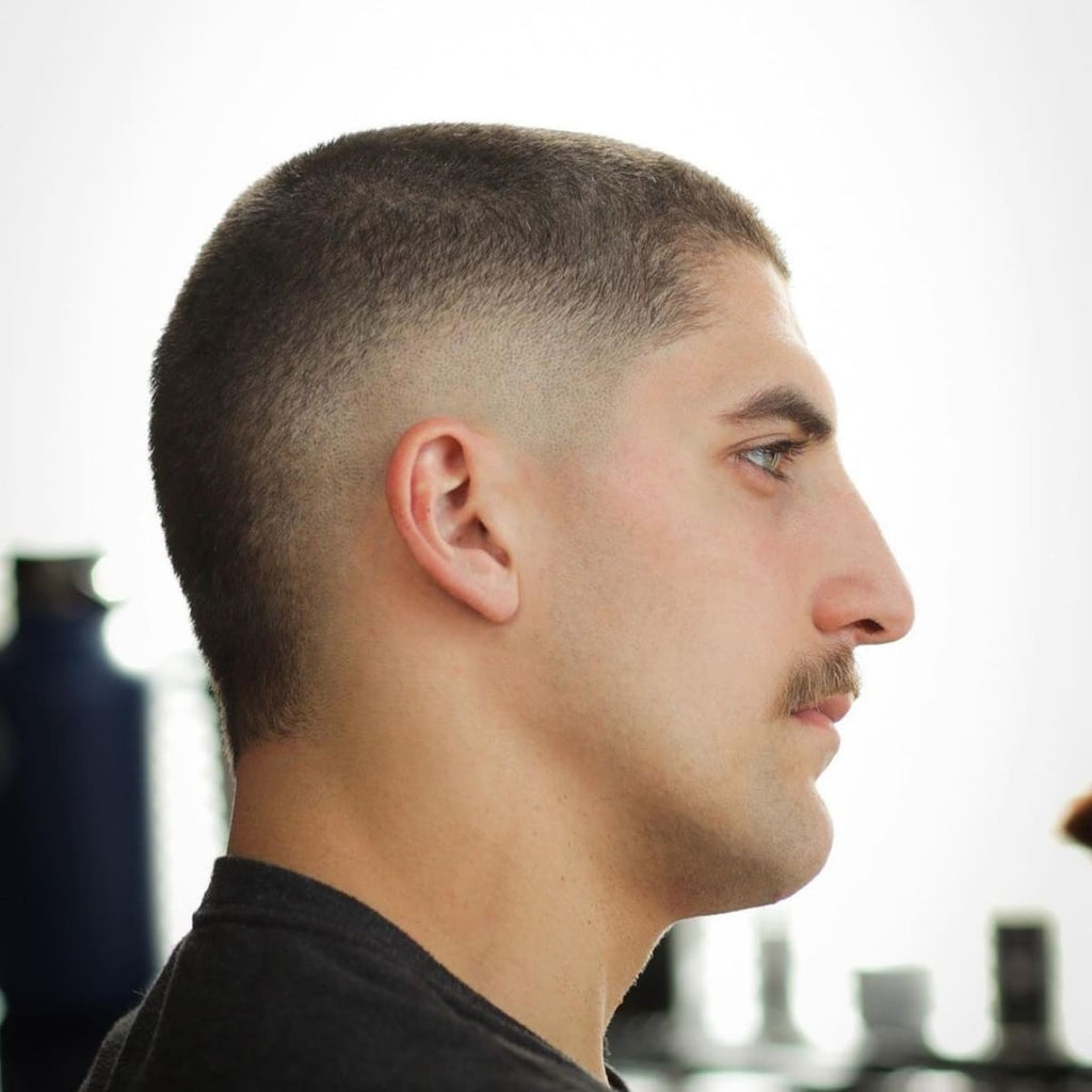 Side profile of a man with a short, low-maintenance crop haircut featuring a smooth fade around the ears. The simple, clean look is paired with a mustache, giving a classic and tidy appearance.