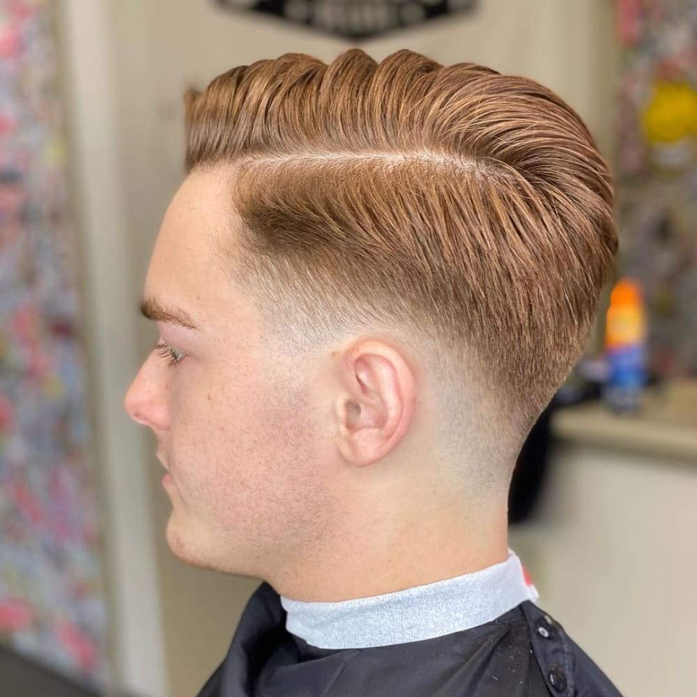 Man with a low skin fade combover haircut, featuring neatly combed-over hair on top with a clean fade down to the skin on the sides and back, showcasing a stylish and professional look for 2024.