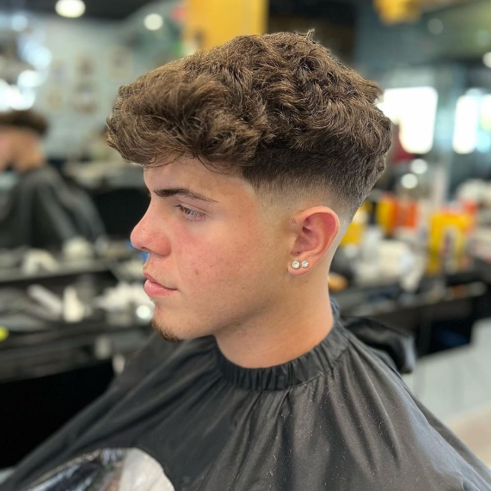 Man with a low fade haircut designed for thick hair, featuring voluminous, naturally curly hair on top and a clean, gradual fade on the sides, showcasing a stylish and modern look for 2024.