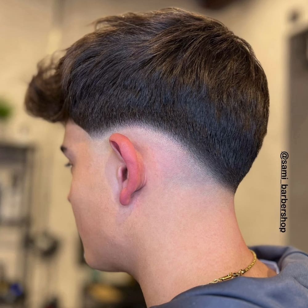 Man with a low skin fade haircut, featuring a sharp fade that transitions smoothly from longer hair on top to skin at the neckline, highlighting a clean and modern style for 2024.