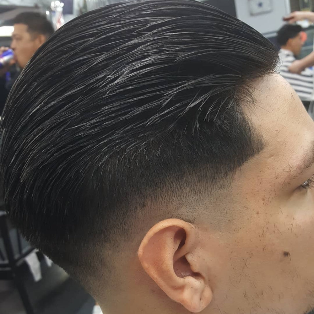 Man with a low skin fade slick back haircut, featuring sleek, combed-back hair on top and a clean, sharp fade on the sides, showcasing a polished and modern look for 2024.