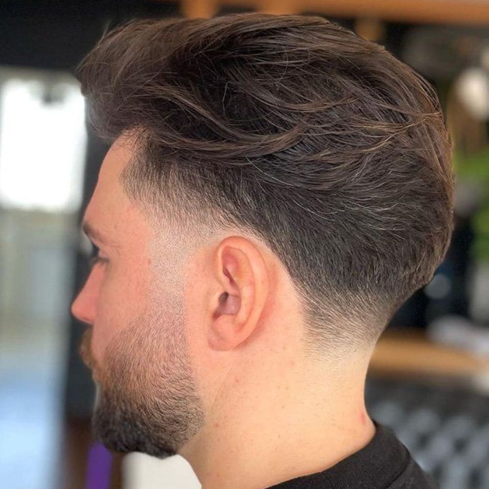 Man with a low fade taper haircut, featuring a smooth, gradual fade on the sides and back with longer, textured hair on top, showcasing a sophisticated and stylish look for 2024