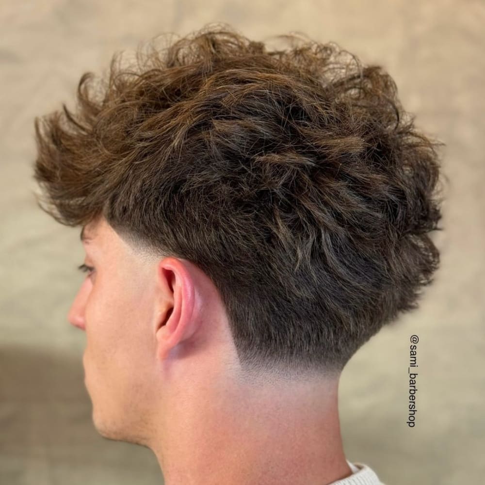 Man with a low taper fade and long top haircut, featuring voluminous, textured hair on top and a clean, gradual fade on the sides, showcasing a stylish and contemporary look for 2024