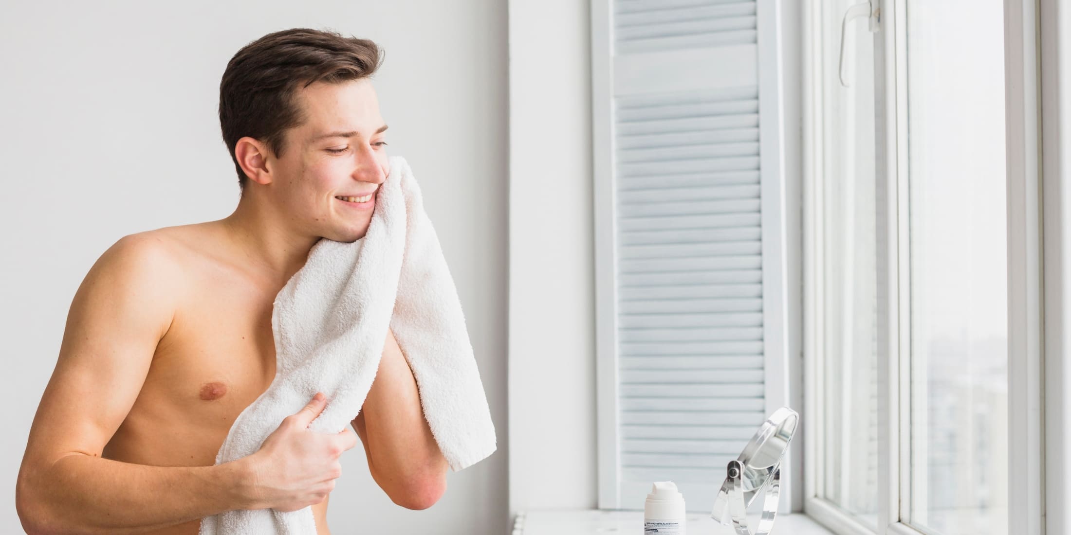 Smiling man drying his face with a towel after shaving, showcasing the benefits of using post-shave balm for smooth and refreshed skin.