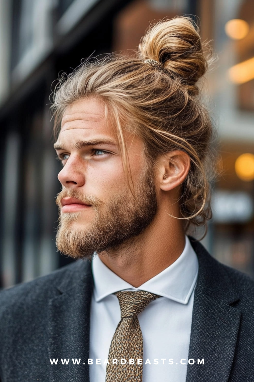 Man with a man bun and a neatly groomed beard, dressed in a formal suit. The man bun is a versatile and stylish option among low maintenance haircuts for men, providing a relaxed yet polished look with minimal daily effort.