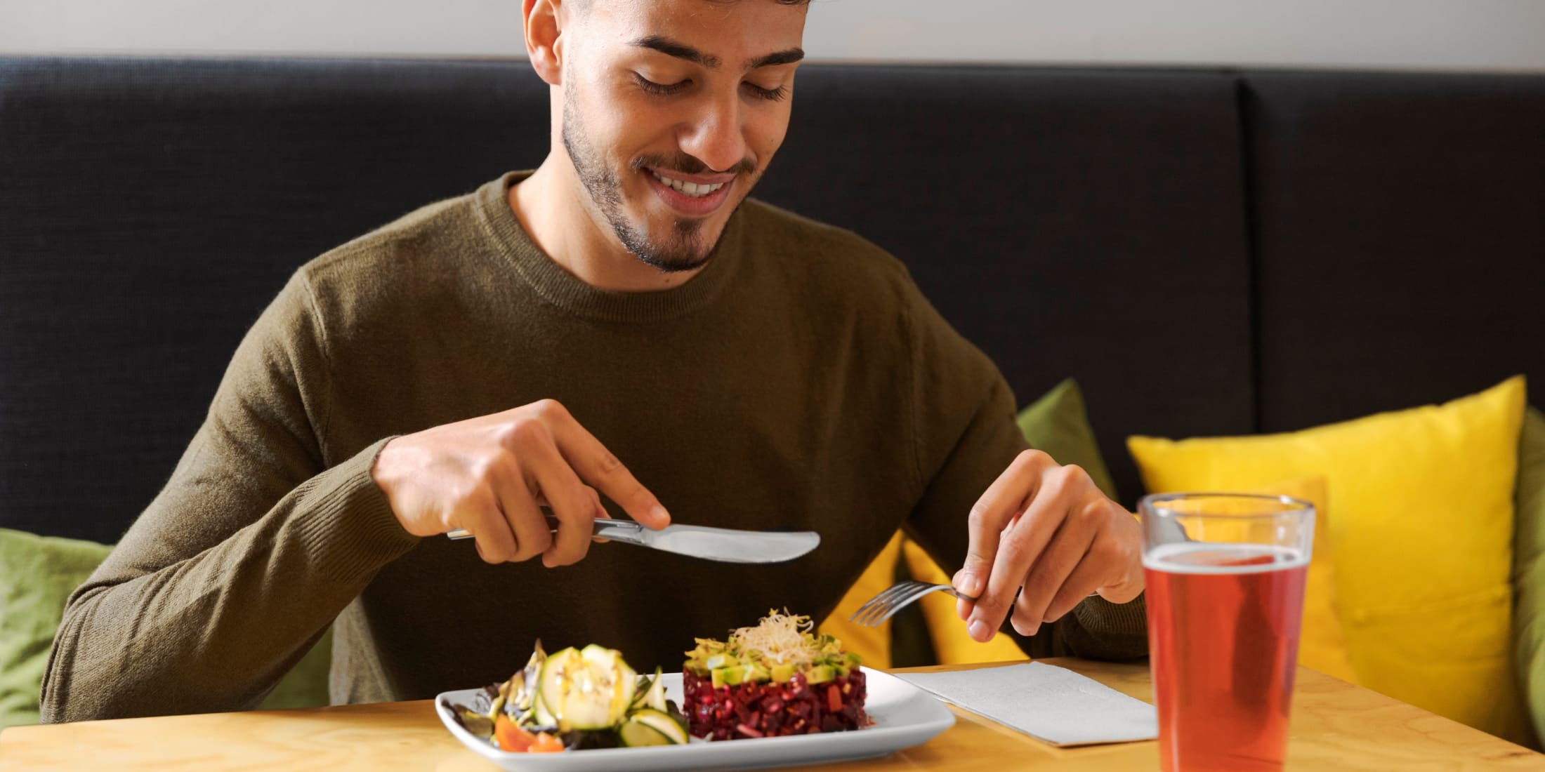 A smiling man enjoys a healthy, balanced meal, emphasizing the importance of good nutrition as part of self-care for men. The plate features colorful vegetables, and he sips on a refreshing drink, highlighting the benefits of a nutritious diet for overall well-being and energy.