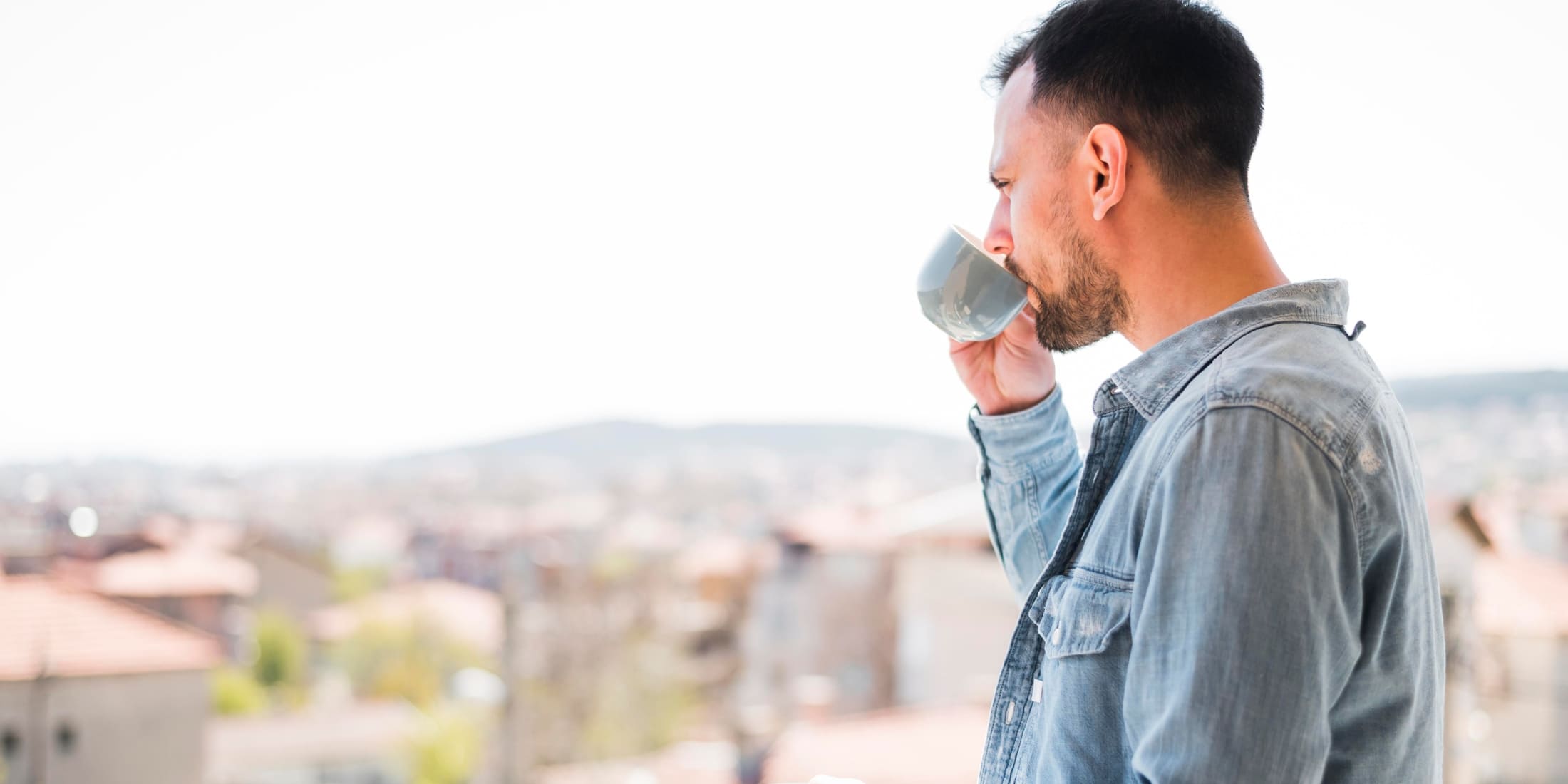 A man sipping coffee while enjoying a peaceful morning view from a balcony. This image captures a calm moment, emphasizing the importance of starting the day with mindfulness and relaxation, a key part of a balanced morning routine for men.