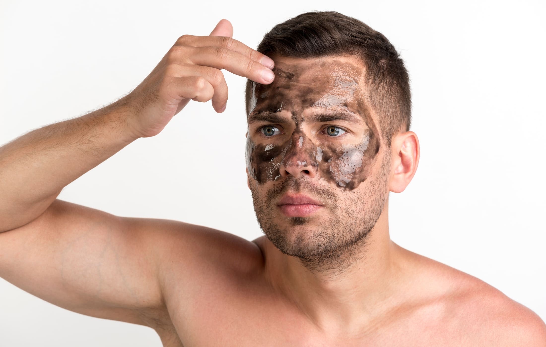 A man applies a dark exfoliating face mask, demonstrating a step in his men’s skincare routine. The mask covers his forehead, nose, and cheeks, focusing on removing dead skin cells and promoting healthy, fresh skin.