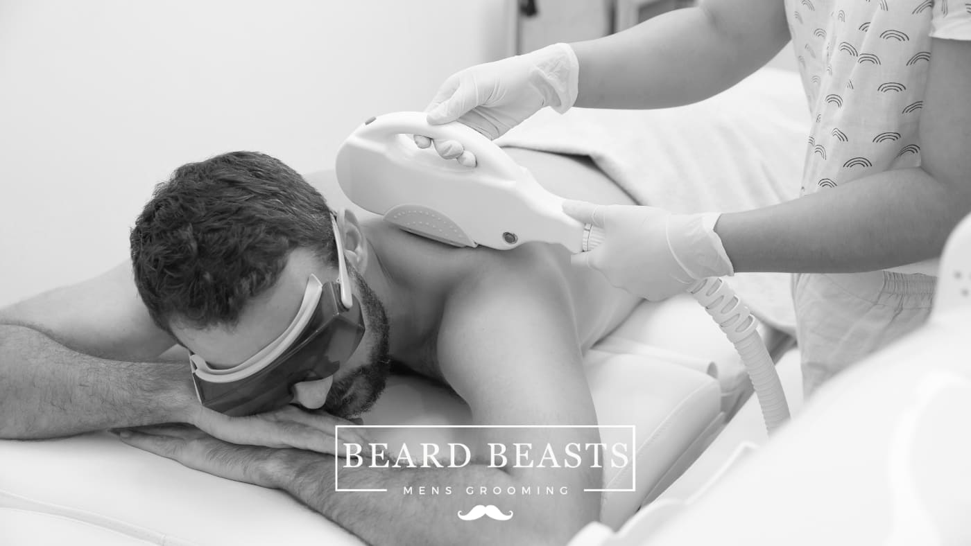 A man lying prone on a spa bed undergoing back hair removal for men with a laser hair removal device, wearing protective goggles