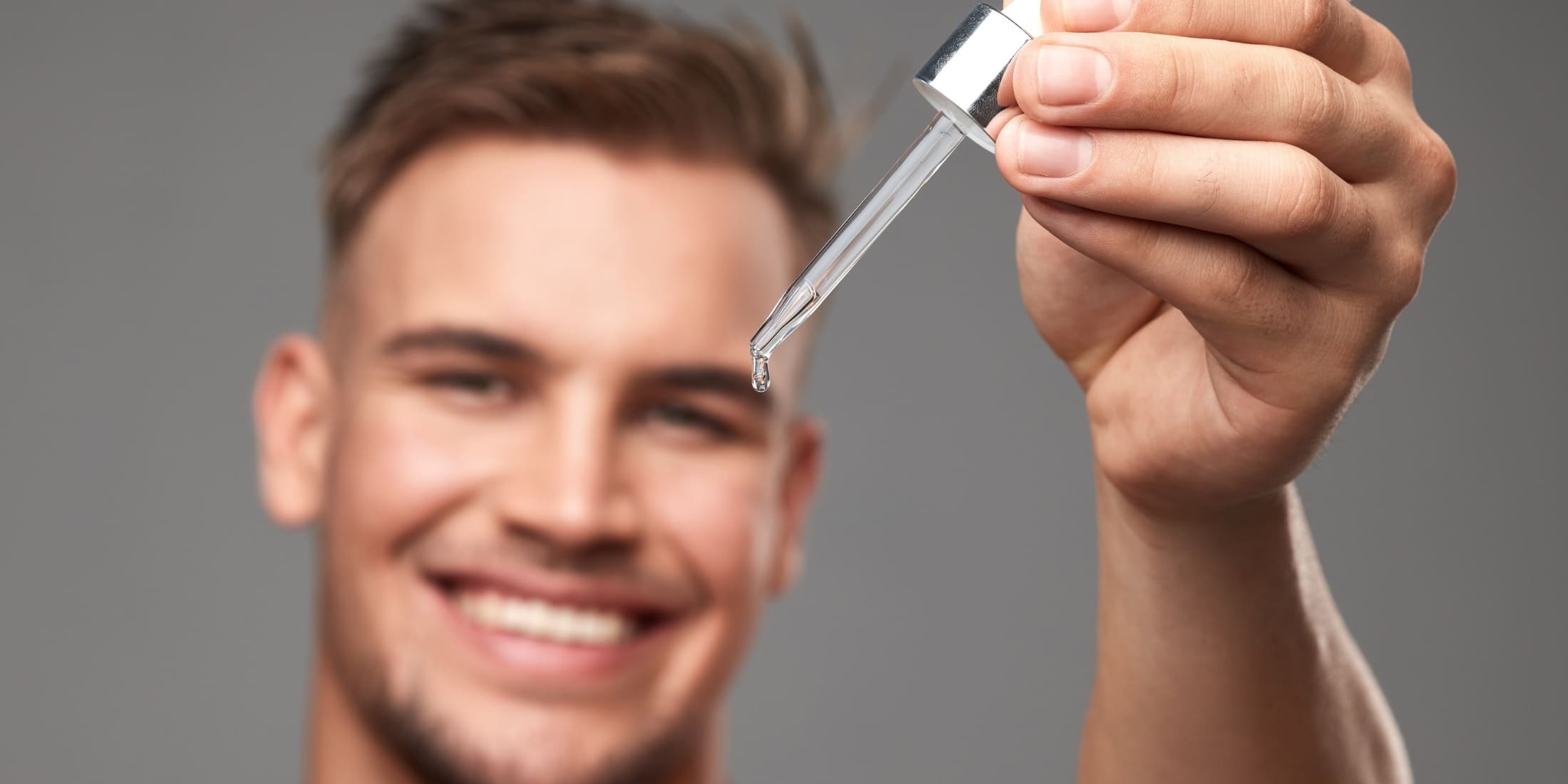 Smiling man holding a dropper with pre-shave oil, demonstrating what pre-shave oil does and how it enhances the shaving experience by softening hair and lubricating the skin.