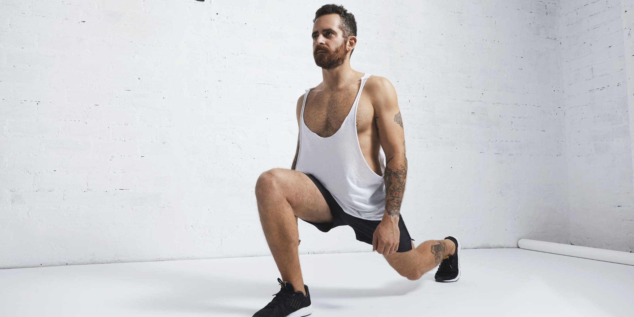 A man in a white tank top and black shorts performing a forward lunge. This exercise targets the legs, glutes, and improves balance. It's a key move in a simple bodyweight workout and ideal for a beginner workout for men, especially in no-equipment morning routines.