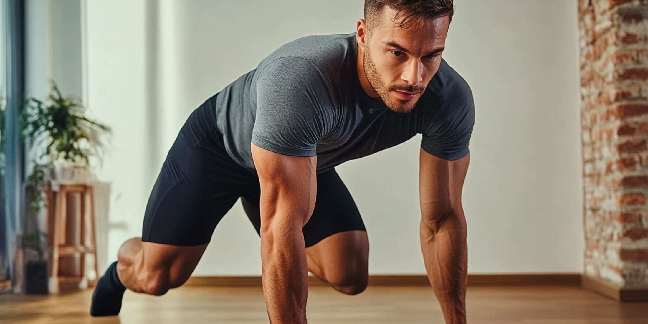 A man performing mountain climbers indoors, wearing a gray t-shirt and black shorts.