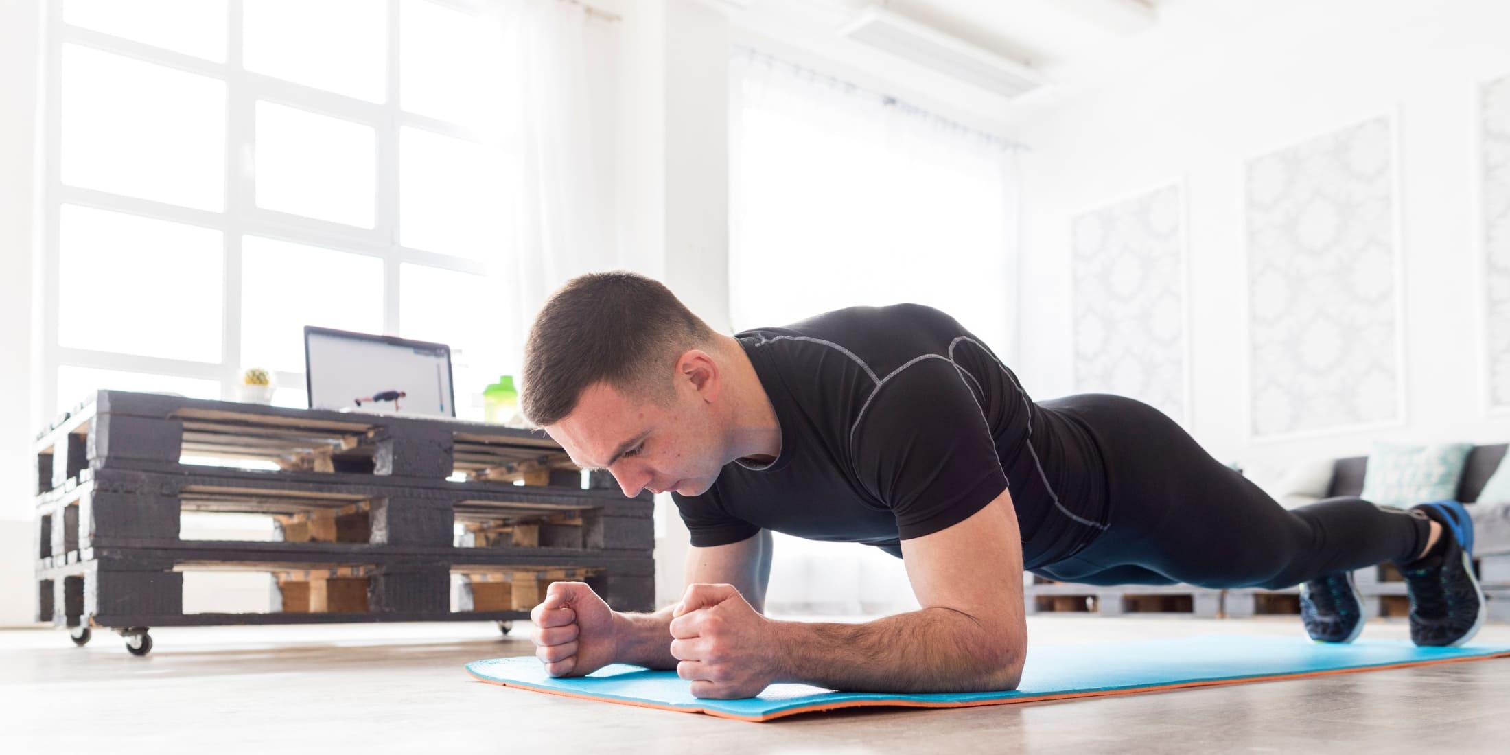 A man in a black athletic outfit holding a plank position on a yoga mat indoors. This bodyweight exercise engages the core, shoulders, and glutes, making it a key move in a simple bodyweight workout or beginner workout for men. Ideal for no equipment morning workouts.