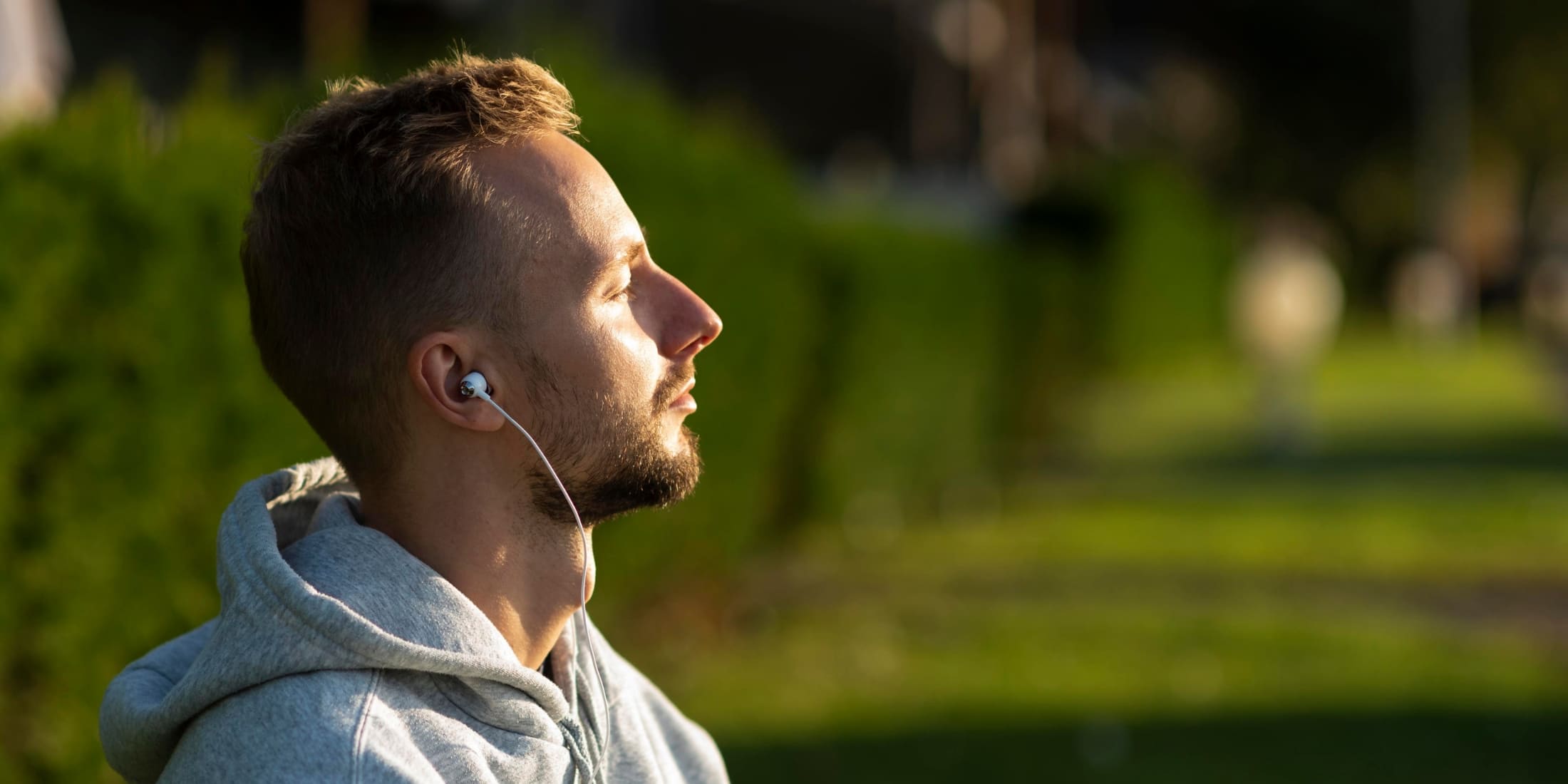 A man sitting in a park, eyes closed and listening to mindfulness meditation through earbuds, enjoying the sunlight.