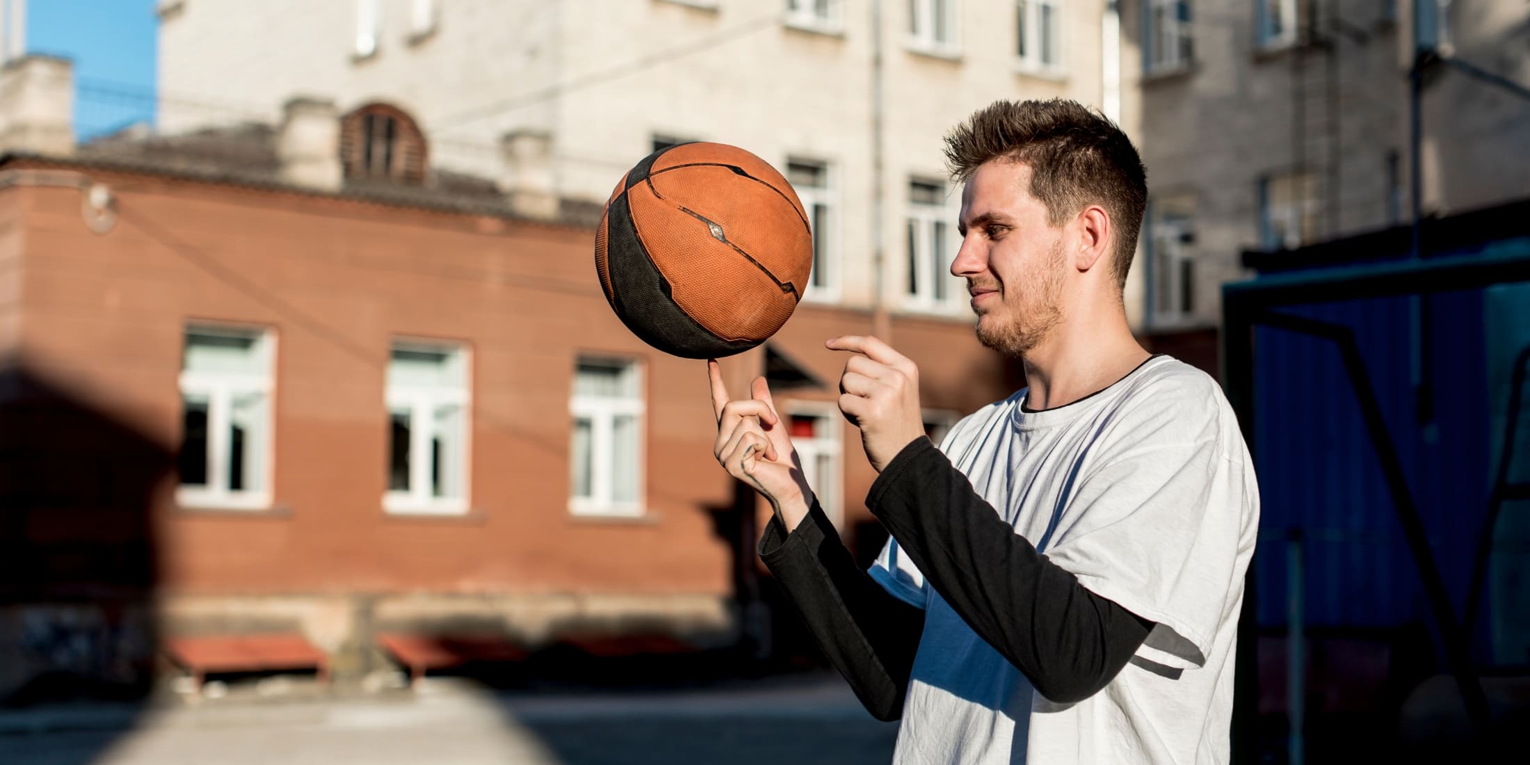 A young man practices spinning a basketball on his finger, enjoying outdoor play. His focus and enjoyment highlight the importance of staying active and engaging in hobbies for mental and physical well-being.