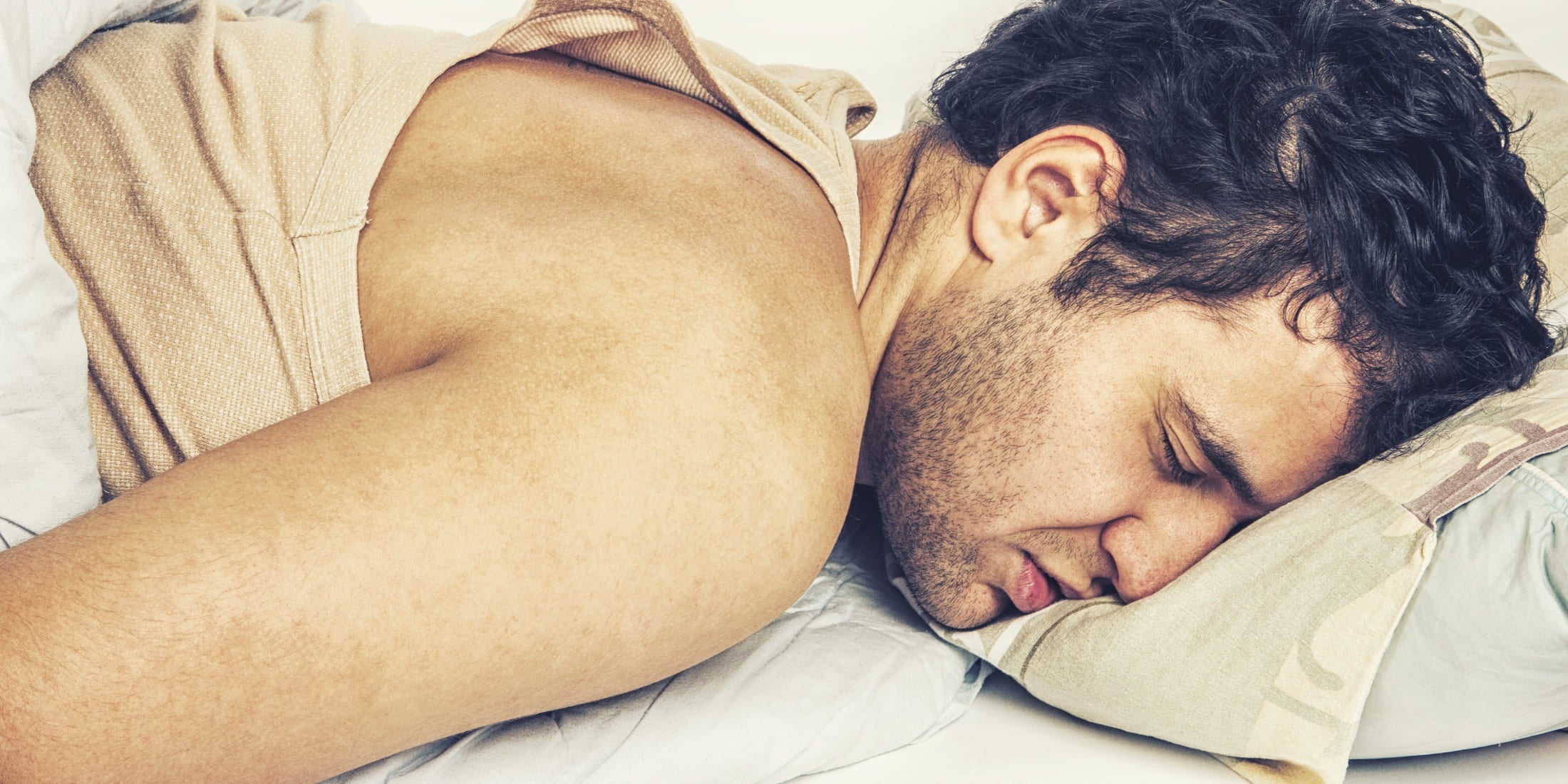 A man deeply asleep, lying face down on a pillow, embodying the struggle to wake up. This image perfectly illustrates the challenge of breaking the snooze habit, a common issue when establishing a consistent and effective morning routine for men.