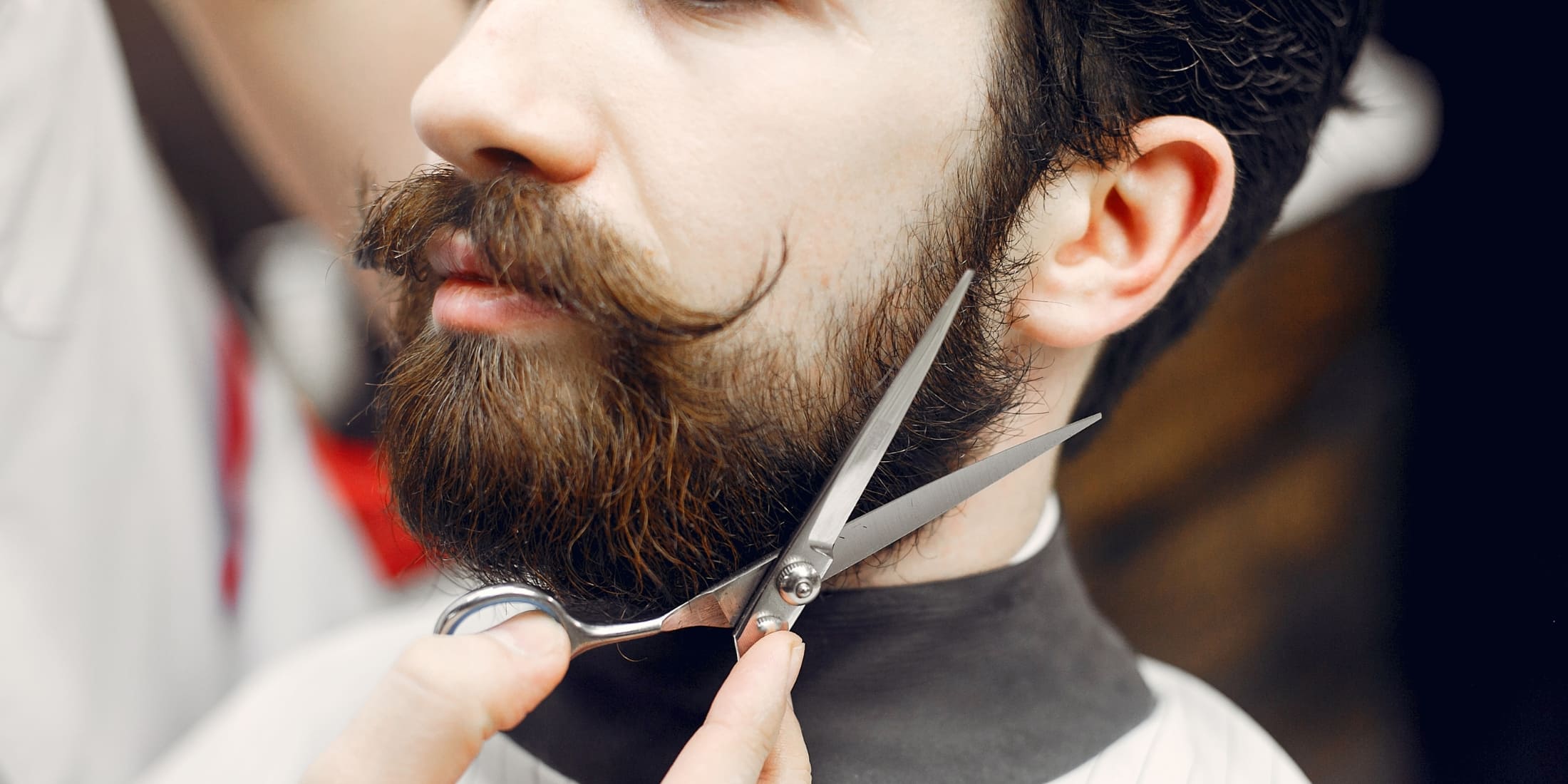 Close-up of a man getting his beard trimmed with scissors, highlighting the precision and care involved in beard grooming. Ideal for articles on beard grooming for beginners, this image emphasizes the importance of regular maintenance and shaping to achieve a well-groomed, stylish beard.