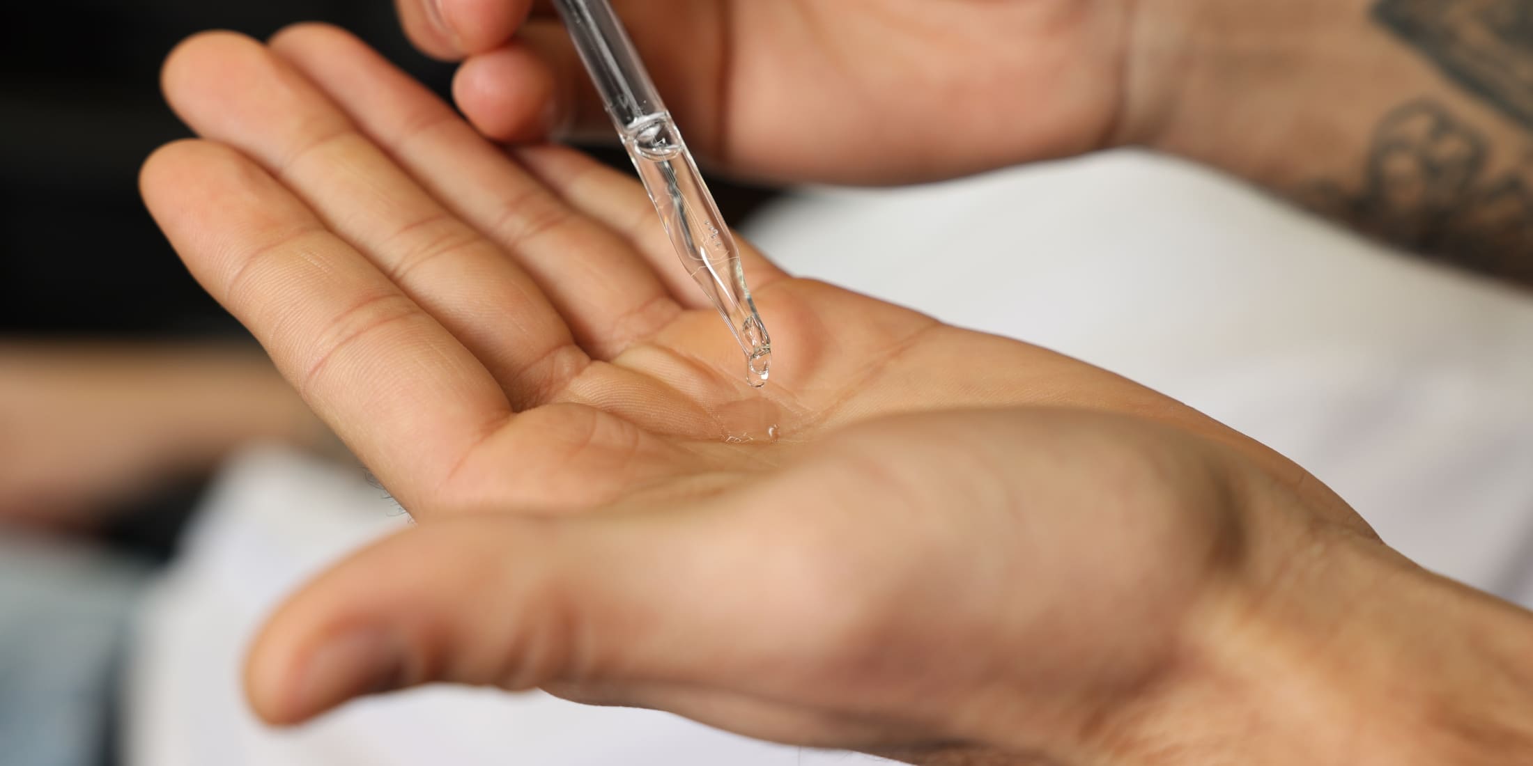 A man's hand being dispensed with clear beard oil from a dropper, demonstrating what beard oil does for your beard in terms of application and grooming.