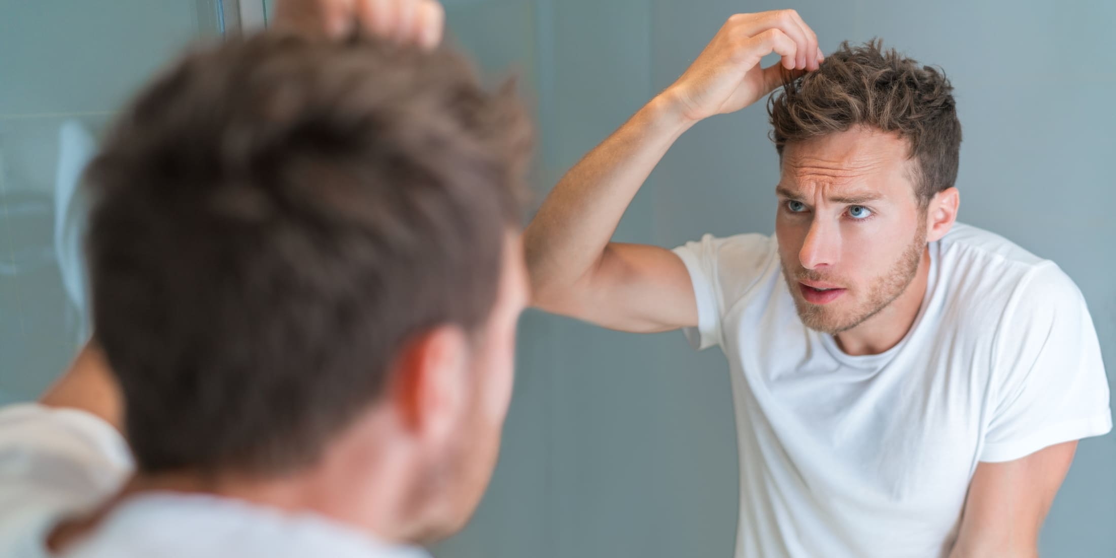 A man looking in the mirror as he styles his hair with hair putty, demonstrating how to use hair putty for a polished look. The man applies the putty to his hair, showcasing its effectiveness in achieving a well-groomed, manageable hairstyle. Perfect for understanding the application process and benefits of using hair putty.