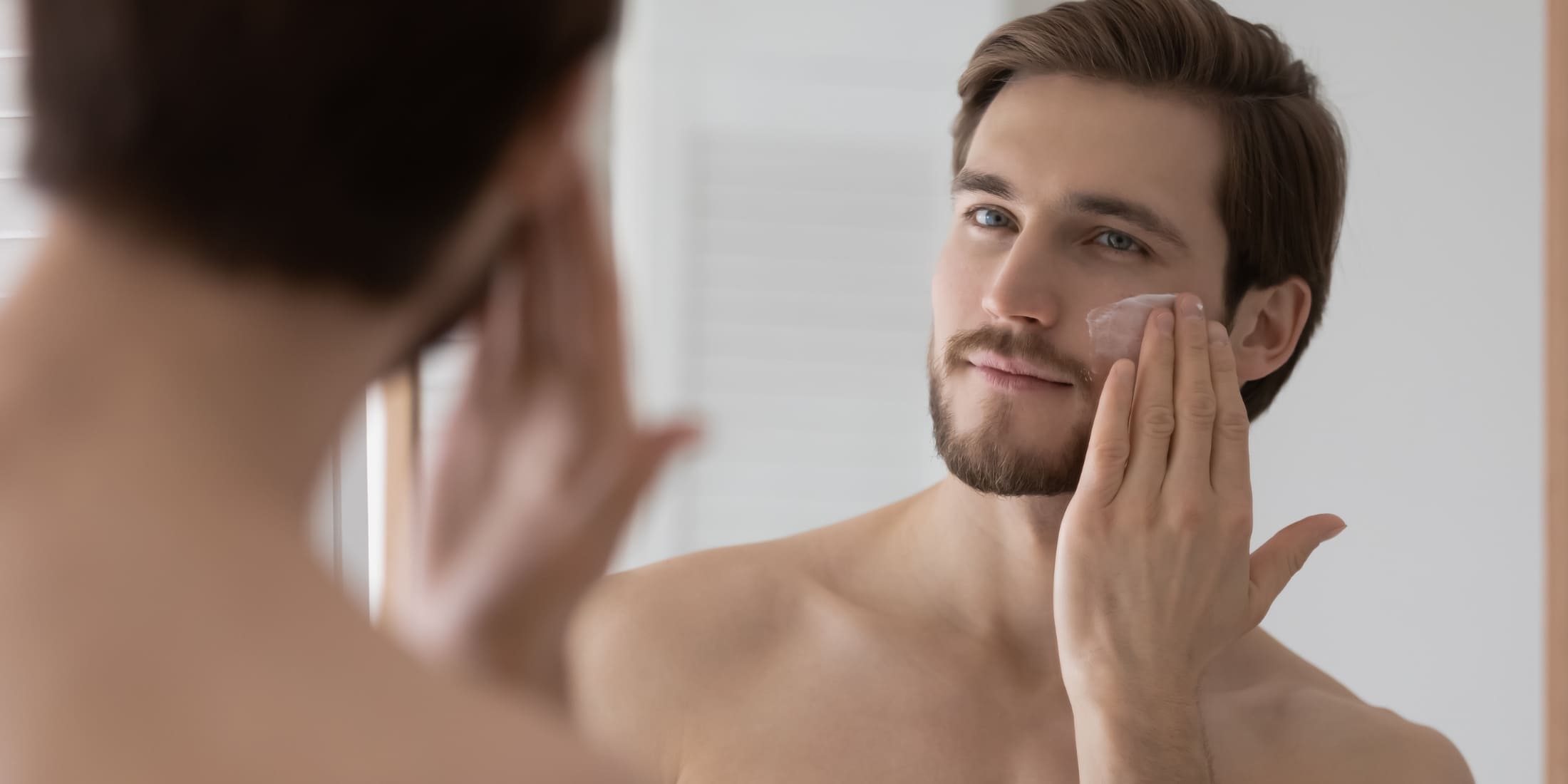 A man applying skincare product while looking into the mirror, highlighting the importance of grooming and self-care in a morning routine for men. This image emphasizes the role of personal hygiene and skincare in boosting confidence and starting the day feeling refreshed.